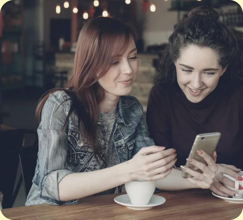 Due persone sedute a un tavolo guardano insieme lo schermo di un telefono
